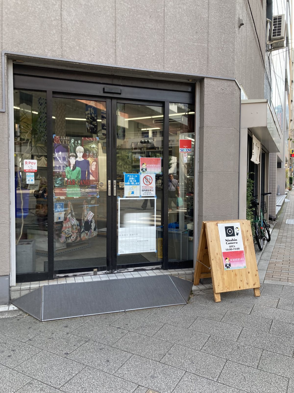 Street-level entrance of Nisshin Camera in Akihabara with a wooden sandwich board in English