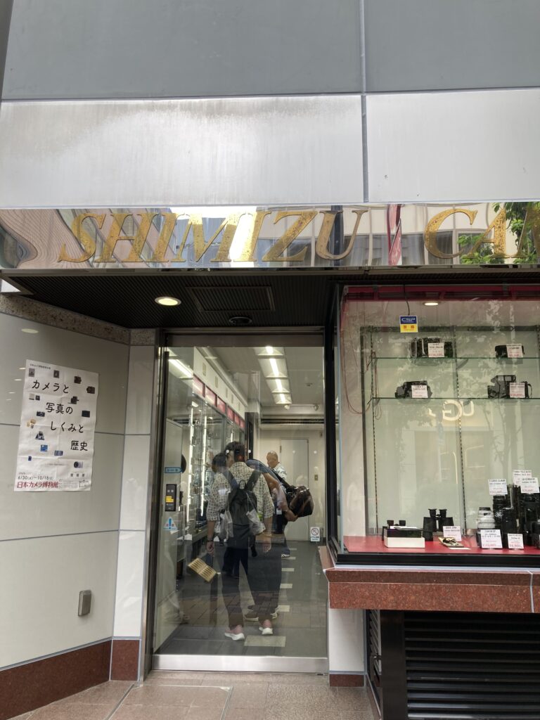 Shimizu Camera shopfront in Ginza, with its sign, priced items in the window and a Japan Camera Museum poster