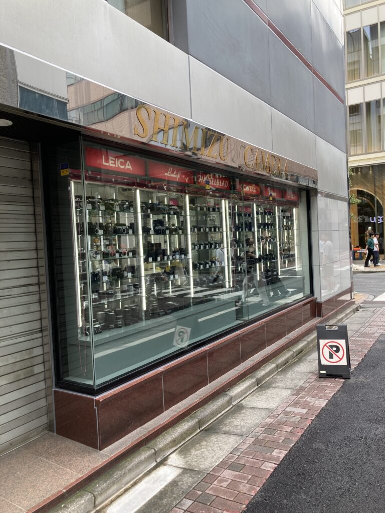 The large street-facing show window of Shimizu Camera, with red maker plates for Leica, Linhof, Hasselblad, Contax, Nikon and Minolta