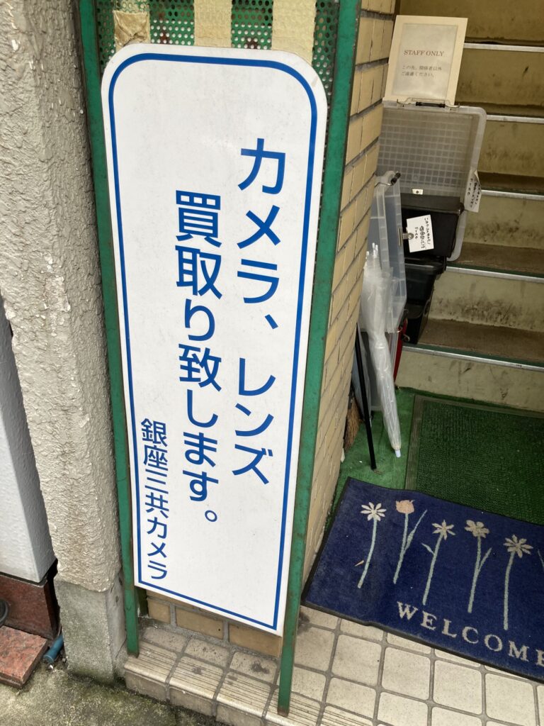 Sankyo Camera stand sign about buying cameras, with a free box by the stairs