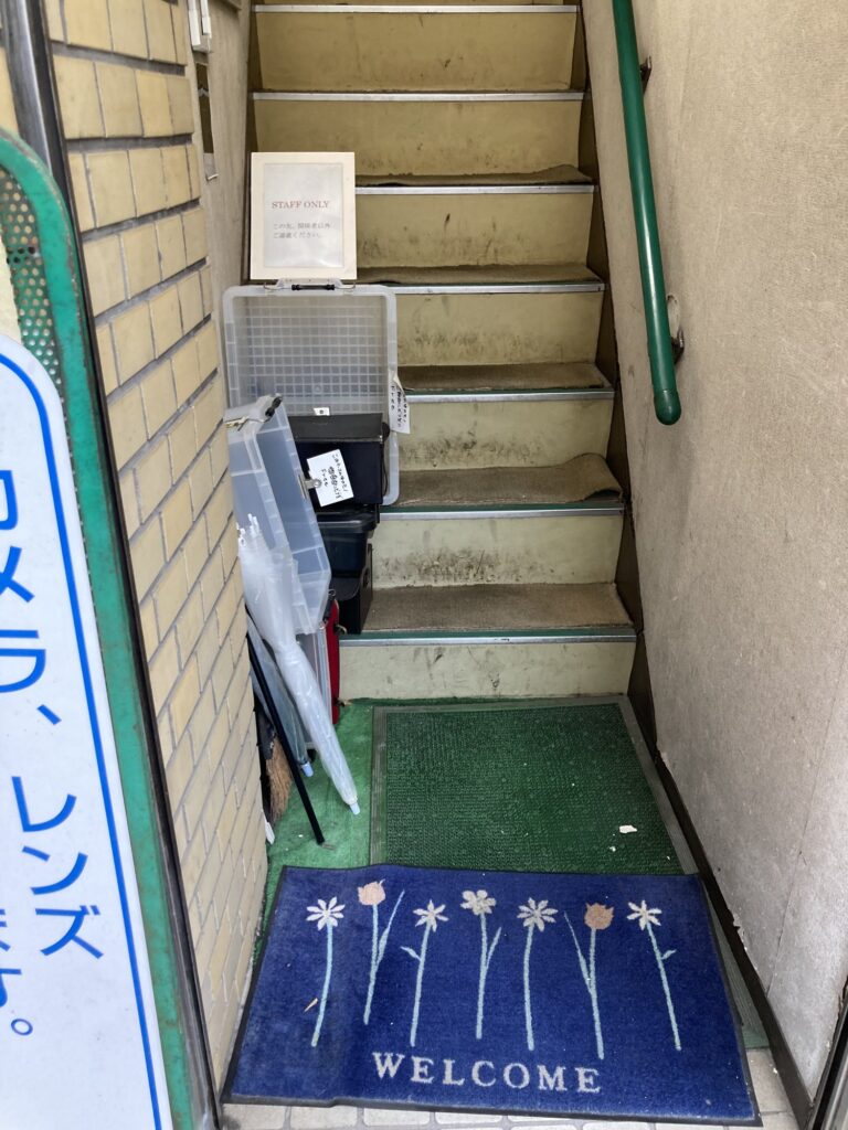 Staff only sign on the stairs beside Sankyo Camera, next to a box of free items