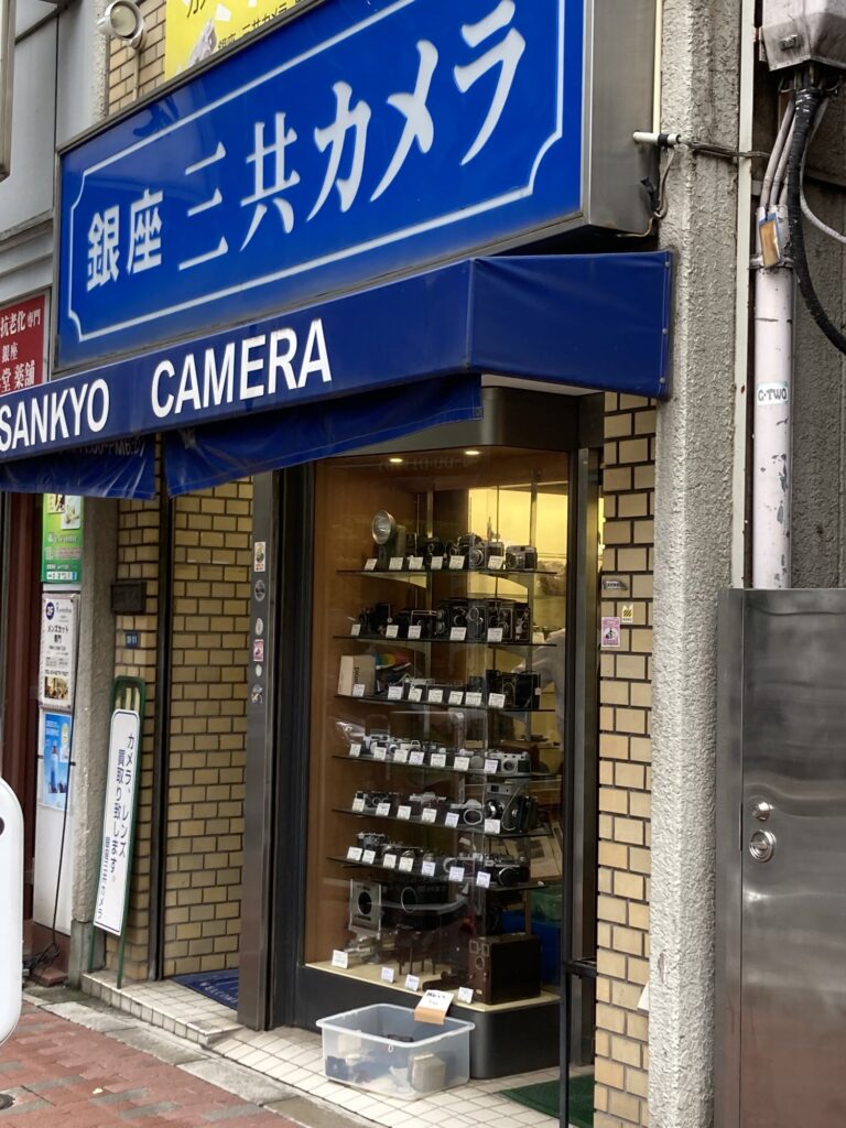 Sankyo Camera in Ginza: blue sign, show window full of classic cameras, and a clear box out front marked Free
