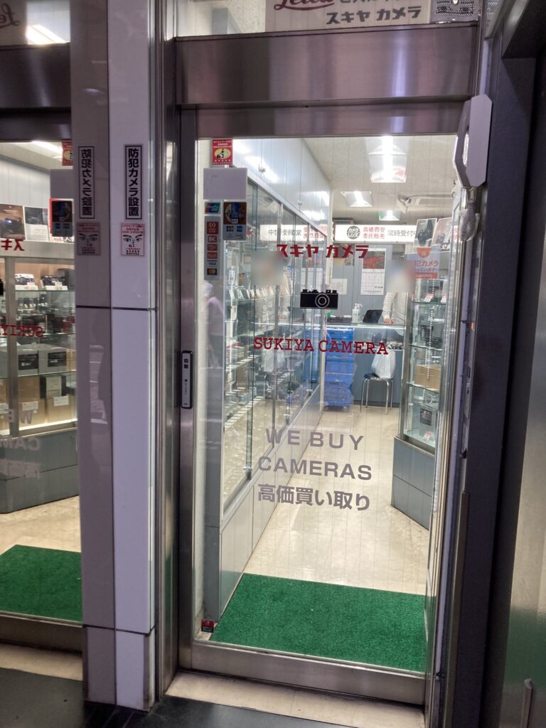 Glass door of Sukiya Camera in Ginza, showing the narrow room of display cases inside