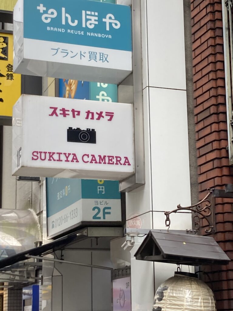 Illuminated white sign reading Sukiya Camera in Ginza, with a camera illustration